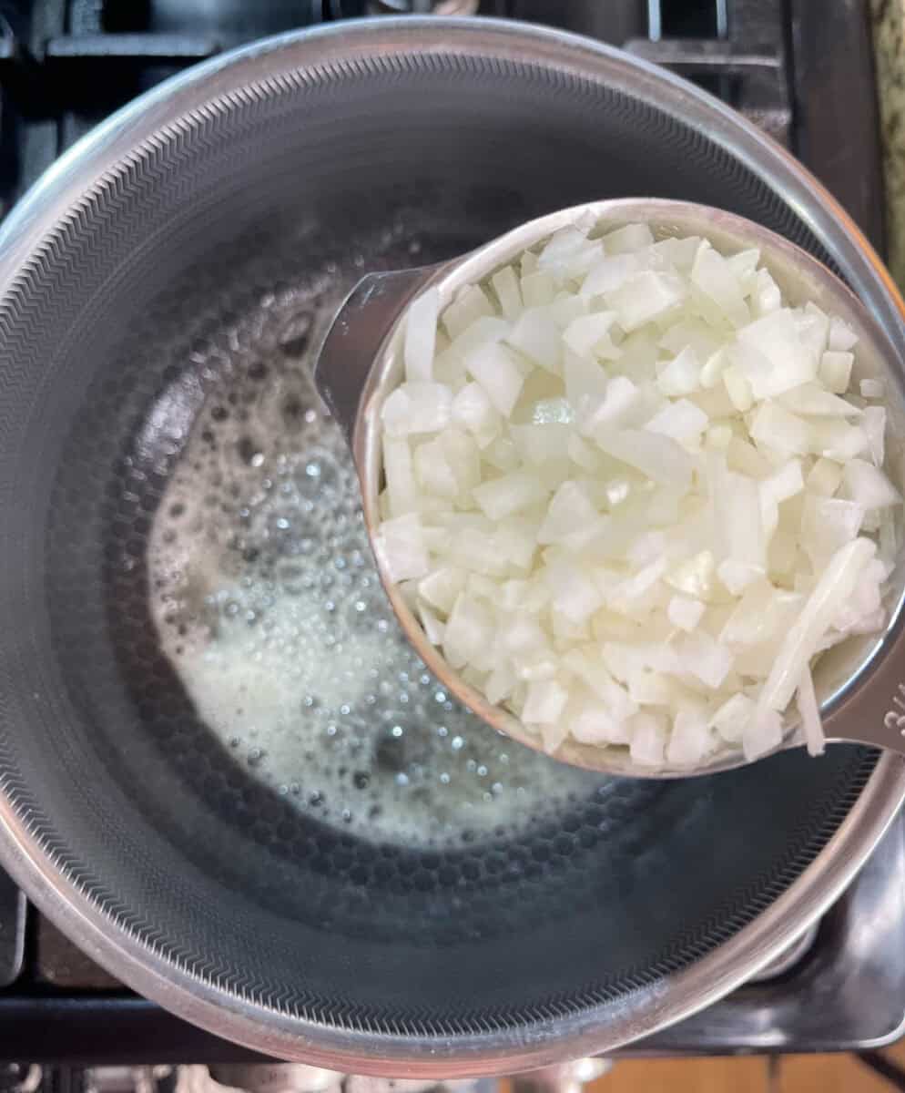adding onion to a pot with melted butter in it