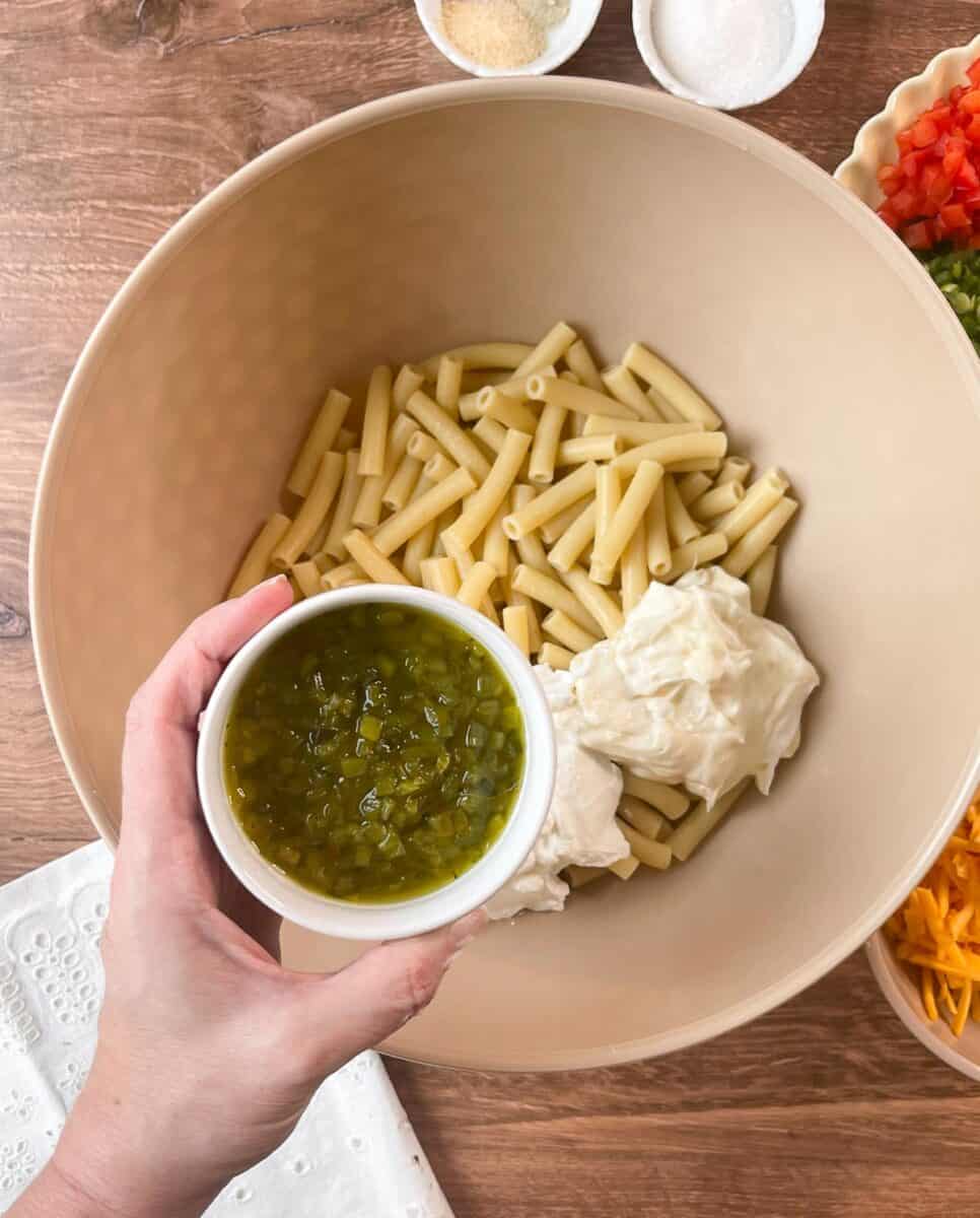 Adding sweet relish to cooked macaroni in bowl