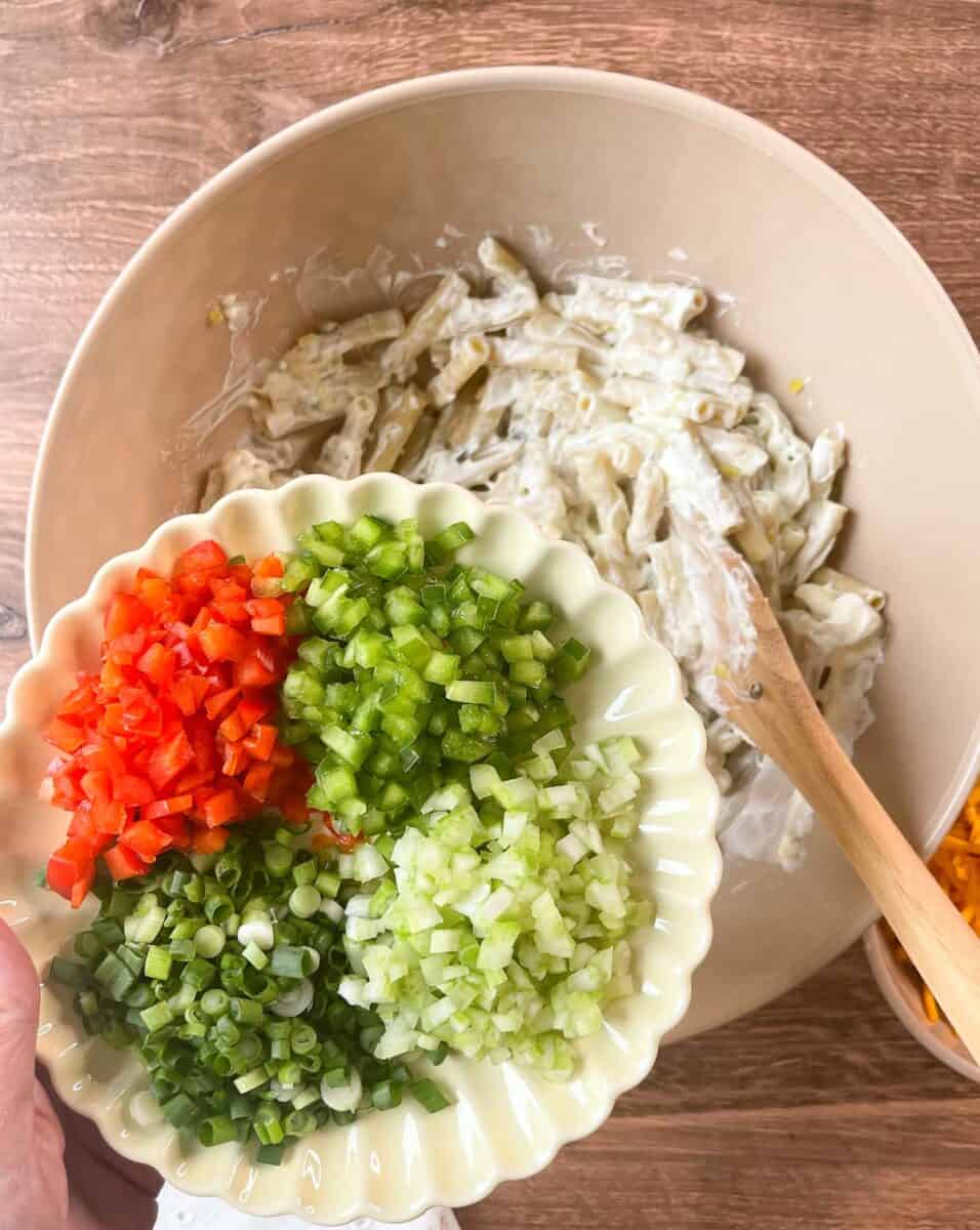 Adding chopped veggies to cooked macaroni in bowl