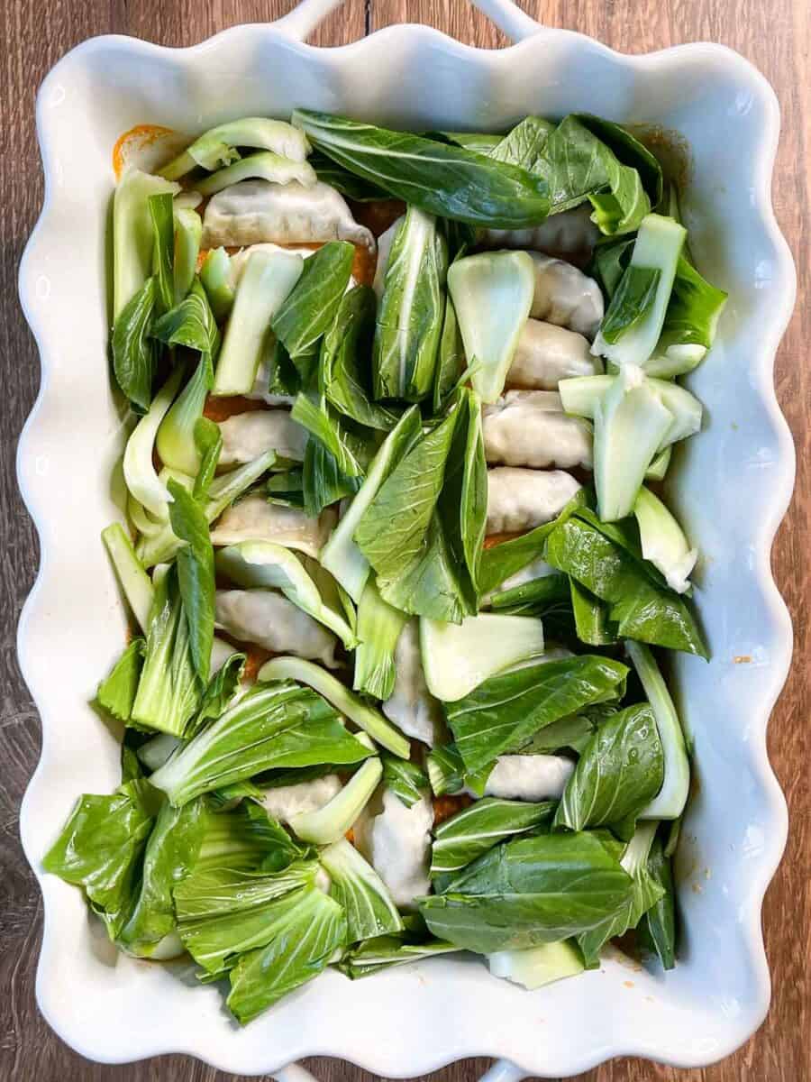 bok choy has been added to the dish around the dumplings